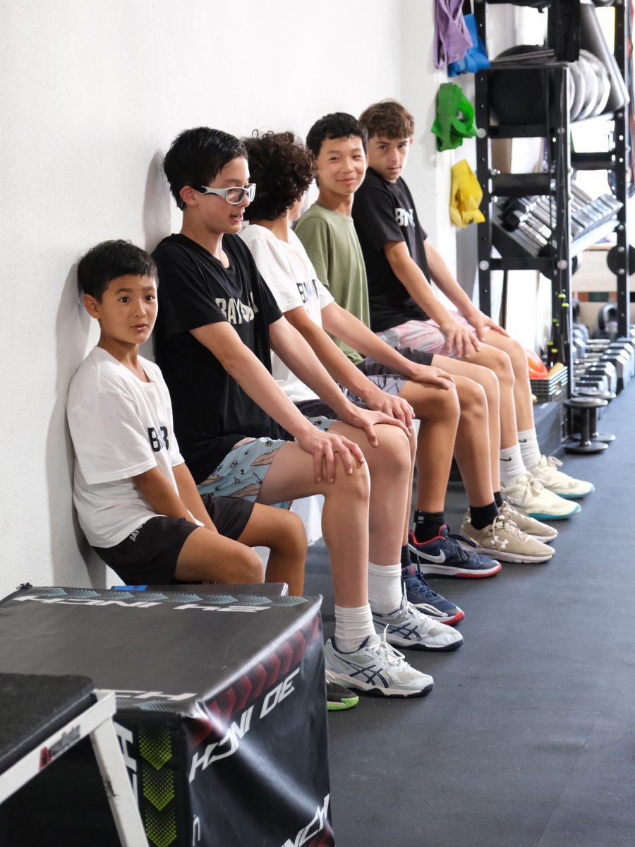 Youth athletes lined up along the wall between sets in a Virtus group class